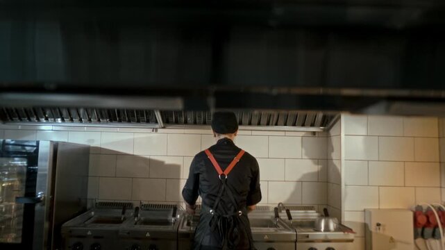Frying chef in uniform works in a commercial restaurant kitchen
