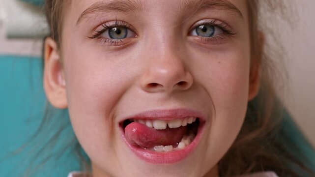 Little girl with brown hair sits in a chair, sticking out her tongue and doing exercises with her tongue at a speech therapist's appointment. Training pronunciation concept. High quality footage