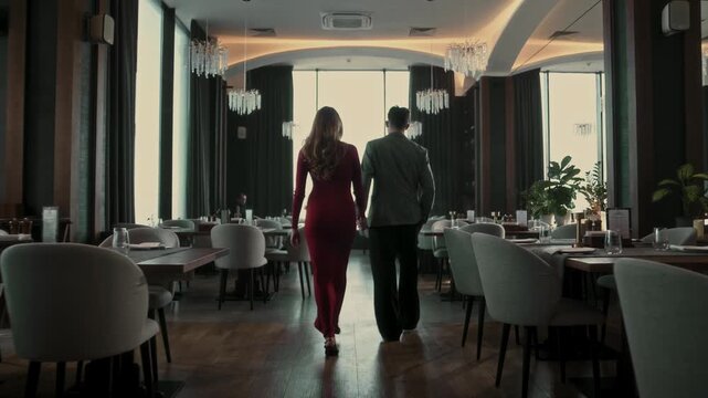 Beautiful young couple walking hand in hand in restaurant interior with panoramic windows
