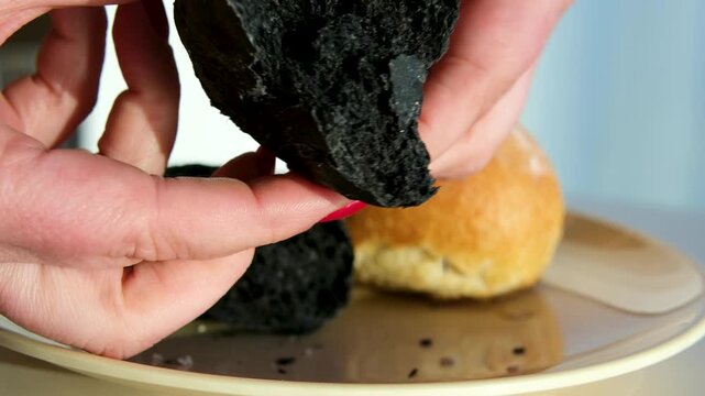 Black bun texture breaking and squeezing soft bread structure close-up bakery product on beige plate food detail concept