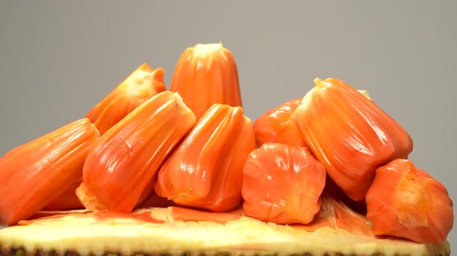 Close-up of ripe red flesh jackfruit bulbs (Mit Ruot Do) spinning smoothly on a piece of rind against a white background. Exotic tropical fruit.