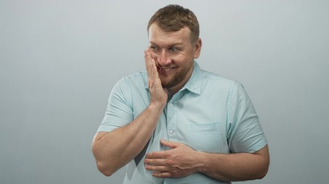 Young caucasian man showing open palms and smiling in studio with pale blue backdrop; playful embarrassment.