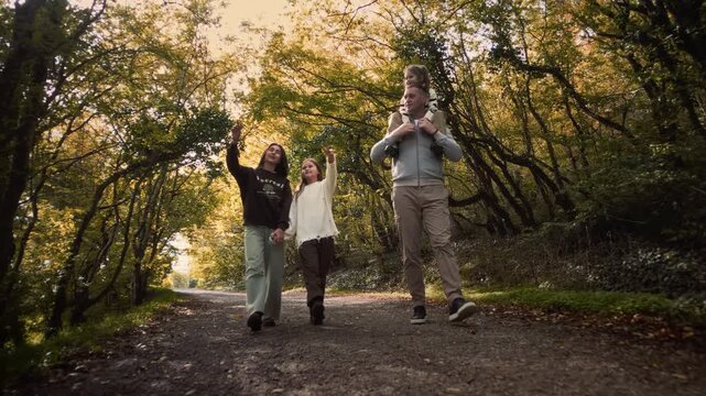 Father mother and two daughters walking through a beautiful autumn forest on a path between the trees in sunny weather during the holidays