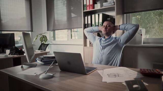 Tired manager in the office reclines in his chair with his hands behind his head and dreams with his eyes closed 