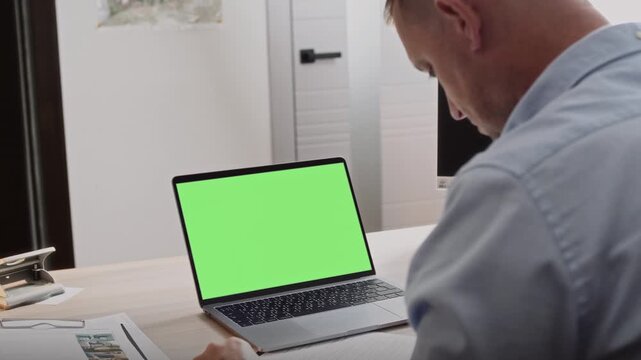 Middle-aged man in a blue shirt sits in an office behind a laptop with a green screen to post your information