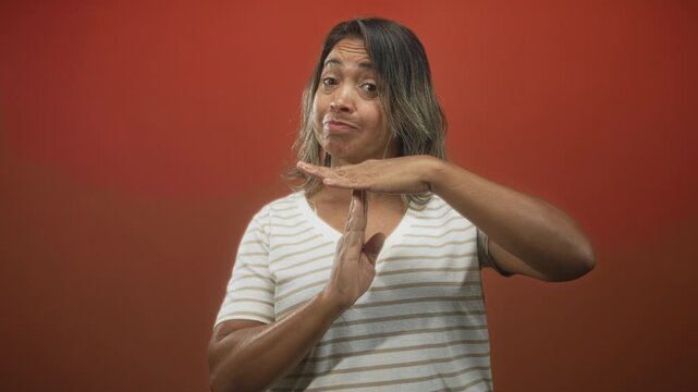 Hispanic woman showing time out hand gesture with visible hands and striped shirt in studio; dismissal boundary.
