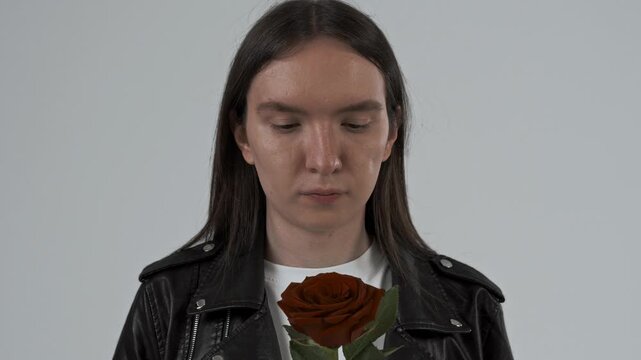 Portrait of a young guy with long hair holding a red rose flower in his hands. White background 