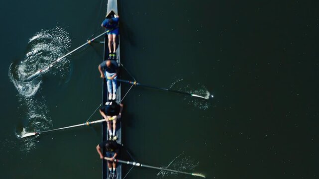 Team of rowers in a boat practicing on calm water in synchronized motion from a drone perspective