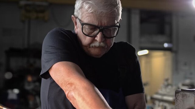 Experienced mature engineer in glasses works on production with his hands at the machine 