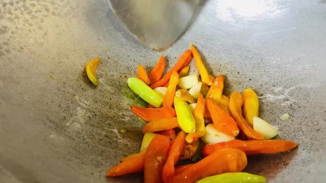 Frying chili and garlic in a pan with a little oil, creating aromatic sambal base, simple home cooking process with sizzling texture and rich traditional flavor.