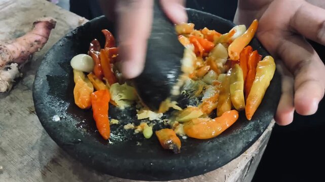Grinding chili and garlic with stone mortar and pestle to make sambal, traditional hand preparation with rich texture, bold aroma, and authentic home cooking process.