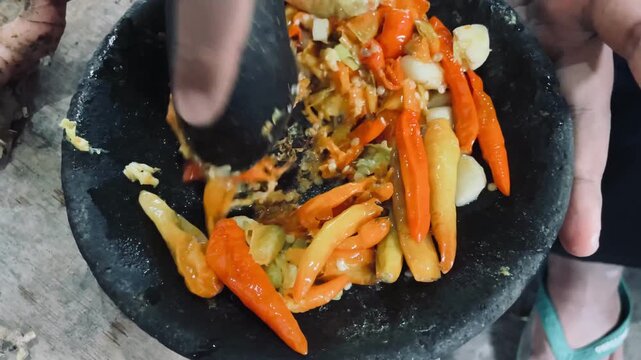 Chili and garlic being crushed on a stone mortar, creating fresh sambal paste with rich texture, bold flavor, and authentic traditional cooking process.