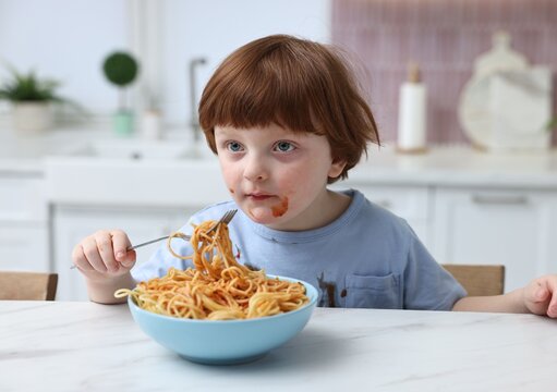 Little boy stained shirt while eating spaghetti at table indoors