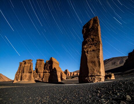 Nightscape of massive yardang monoliths in remote desert with horizontal star trails. Sharp volcanic stones, geometric rock formations, and deep focus with copy space. Desert nature concept.