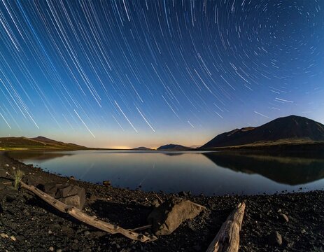 Lake Bulunkul in Tajikistan at night with horizontal star trails. Sharp volcanic rocks, still water reflection, and starry sky with deep focus and copy space. Pamir Mountains nature.