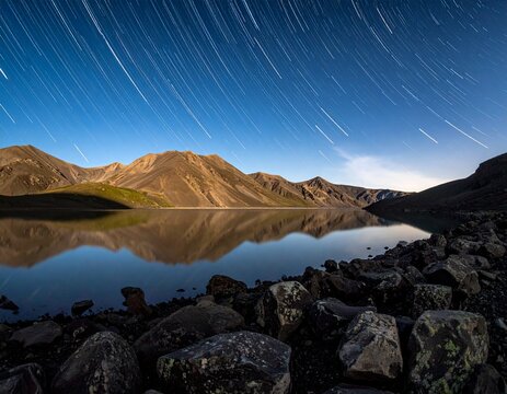 Lake Bulunkul in Tajikistan at night with horizontal star trails. Sharp volcanic rocks, still water reflection, and starry sky with deep focus and copy space. Pamir Mountains nature.