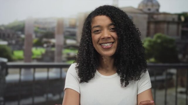 Woman smiling with crossed arms at roman building with stone ruins in bright midday sunlight; confidence.