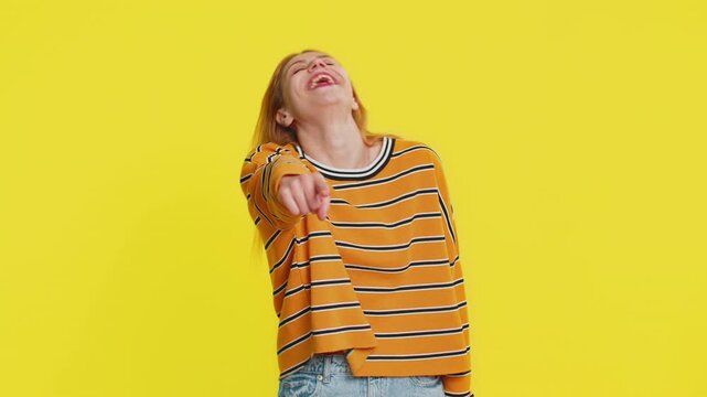 Caucasian woman pointing finger to camera, laughing out loud, taunting making fun of ridiculous appearance, funny joke anecdote, bullying, abuse. Young adult girl isolated on yellow background indoors