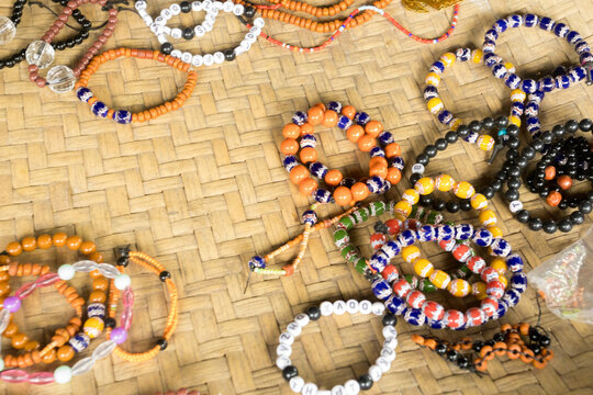 Bracelets and necklaces made from various materials, in different styles and colors, are displayed on winnowing trays and serving trays in a traditional Sumba village.