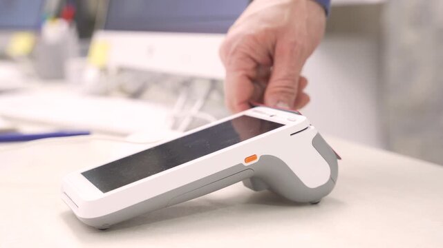 Customer hand holding a credit card to pay via a modern POS terminal in a clinic or cafe