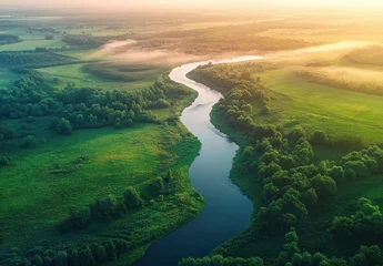 Fototapete Nebliger Morgen aerial view of a winding river through green fields and dense trees at sunrise with soft morning mist, peaceful and serene atmosphere  © Donna