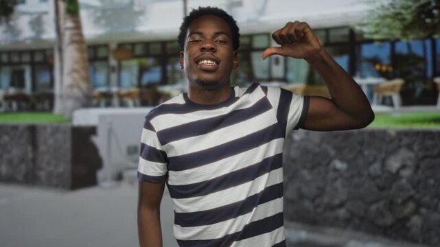 Man pointing thumb to chest outside modern building under bright sunlight on urban street; self identity confidence.