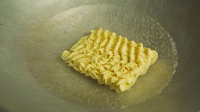 Dry instant noodles being dropped into a metal wok filled with bubbling boiling water.
Dry instant noodles being dropped into a metal wok filled with bubbling boiling water.

