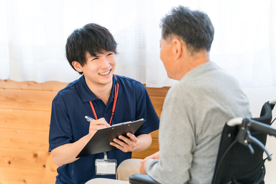 A male caregiver interviews a senior man in a wheelchair.