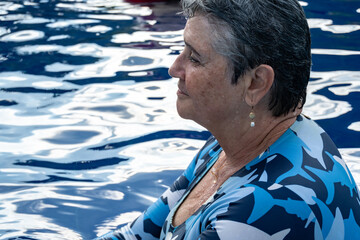 Profile portrait of a happy senior woman with short gray hair smiling in a swimming pool, active aging and healthy retirement lifestyle concept, summer vacation at a luxury resort © Sergio Palacio