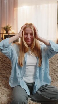Young woman sits at home with hands near head shouting wow in genuine shock over sudden idea. Caucasian girl on sofa expresses mental explosion revealing big emotional surprise under sunset happy news