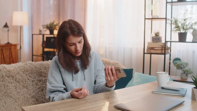 Young Caucasian woman plugging charging cable into smartphone and unplugging it repeatedly as charger fails to work. Girl appears frustrated noticing cable is broken and unable to charge device.