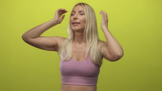 Woman wearing purple sports top plugs fingers into ears with eyes closed and slight frown in green studio setting; annoyance.