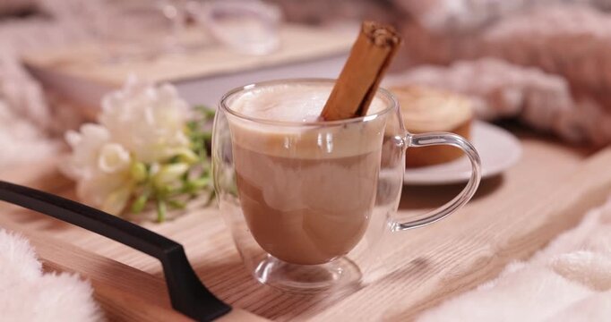 Aromatic coffee with cinnamon stick in cup, tasty tart and flowers on bed, closeup. Camera moving backwards