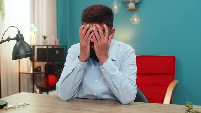 Indian man at home hides face devastated by breakup bankruptcy job loss future uncertain lonely. Arabian guy at table wrestles sorrow shaken by financial ruin heartache and stress tears unseen inside.