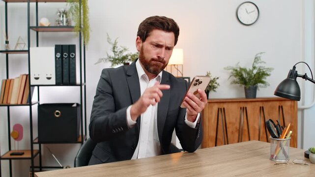 Middle-aged businessman at home office spends money on online lottery casino smartphone app groans as luck fails. Freelancer guy slams fist hard exhales heavy drops head on hands after gambling loss