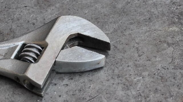 Steel adjustable wrench head resting on a dirty metal workshop table. Close-up of industrial hand tool for turning nuts and bolts in a professional mechanical garage environment.