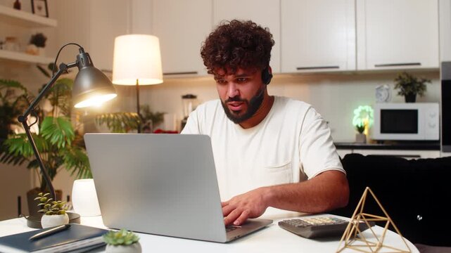 Arabian man at home in headset with microphone helps client on chat and phone writes ticket. Egyptian guy sitting at table asks short questions confirms issue gives steps records solution sends email.
