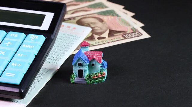 黒背景で回転する1万円札と通帳と電卓とミニチュアハウス