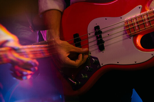 Close-up of hands playing red electric bass guitar on stage