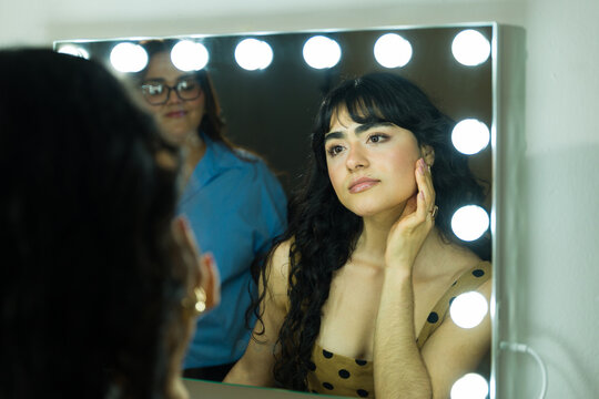 Beautiful Hispanic model reflecting her face in a lighted vanity mirror backstage while she gets her makeup done