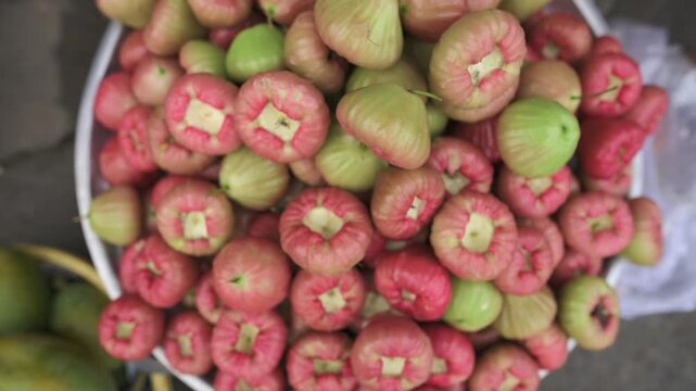 Overhead Bowl Rose Apples Display, Chef Selecting Glossy Pink Green Fruits At Busy Vietnamese Street Market, Crisp Skin, Starshaped Calyx Visible, Seasonal Harvest Presented On Metal Tray