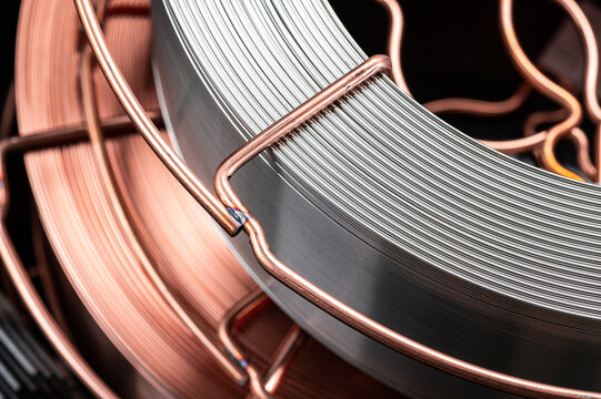 Copper and steel welding wire spools close up. Detailed view of coiled metal welding wire on industrial spools with copper coating and silver finish.