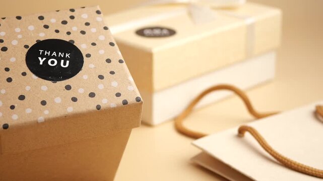 Close up motion of elegant craft gift boxes and shopping bags on beige background with thank you sticker.
