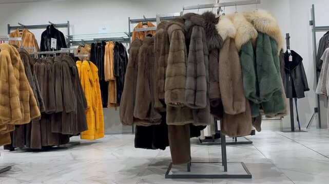 close-up coat rack showcasing fur coats in boutique: brown and green fur jackets clustered on metal rack, bright yellow parka in background, polished concrete floor,