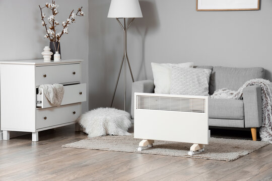 Interior of stylish living room with modern electric convector heater and grey sofa