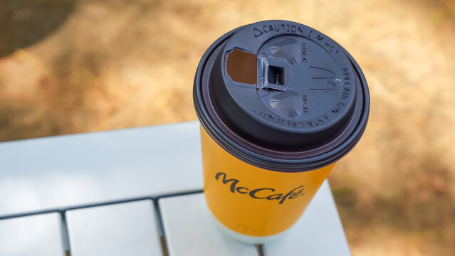 McCafe coffee cup with lid placed on a white table outdoors, blurred natural background with soft lighting and warm tones