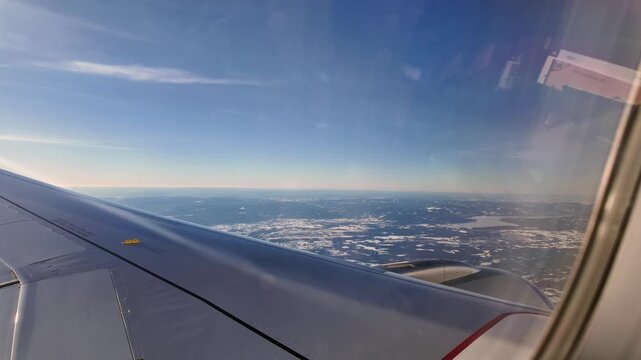 A view out the window of a Scandinavian Airlines aircraft flying low over a winter landscape on approach to Oslo Airport Gardermoen.