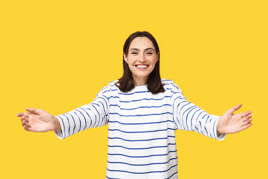 Young woman opening arms for hug on yellow background