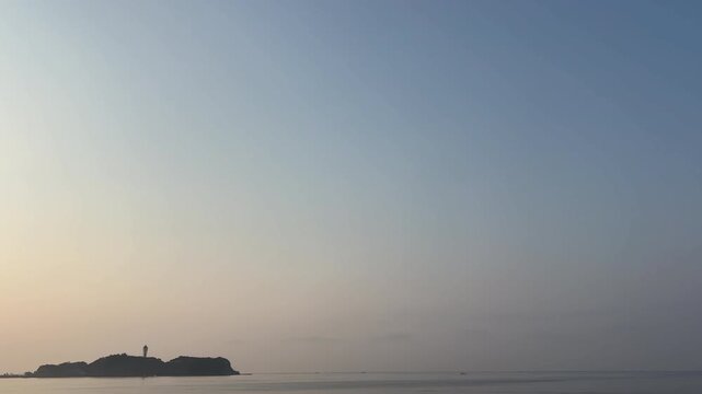 朝焼けと晴れた空の淡いグラデーションと静かなと灯台のある島