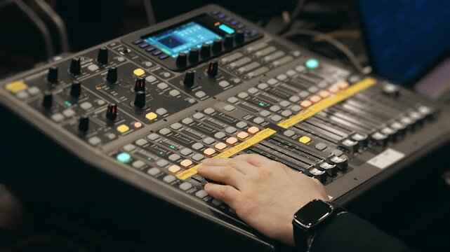 Close up of audio engineer hand adjusting controls on sound mixing console in recording studio environment.